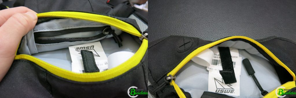 No lado esquerdo da imagem, bolso resistente à água com zíper. No lado direito, gancho de velcro e saída para cabos/fones de ouvido.