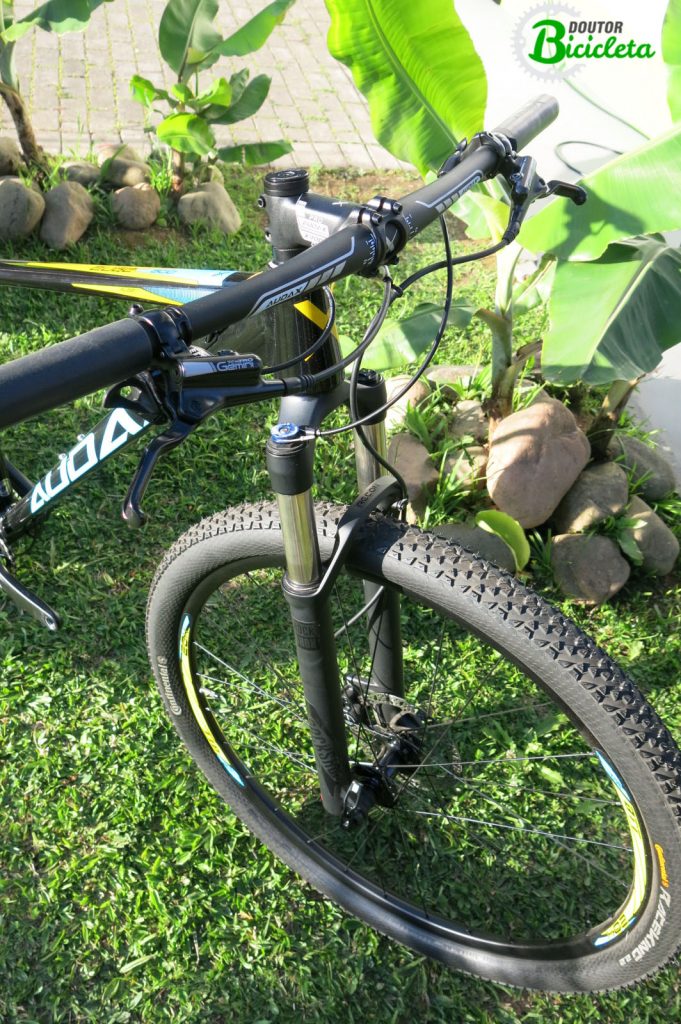 Aros de 29", freios hidráulicos, suspensão dianteira Rock Shox Recon a ar com trava no guidão e ajuste de retorno.